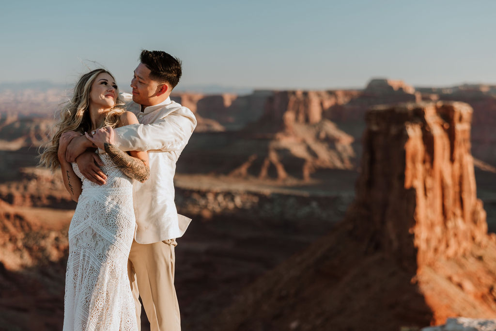 couple embrace along ledge overlooking Moab's rocky landscape