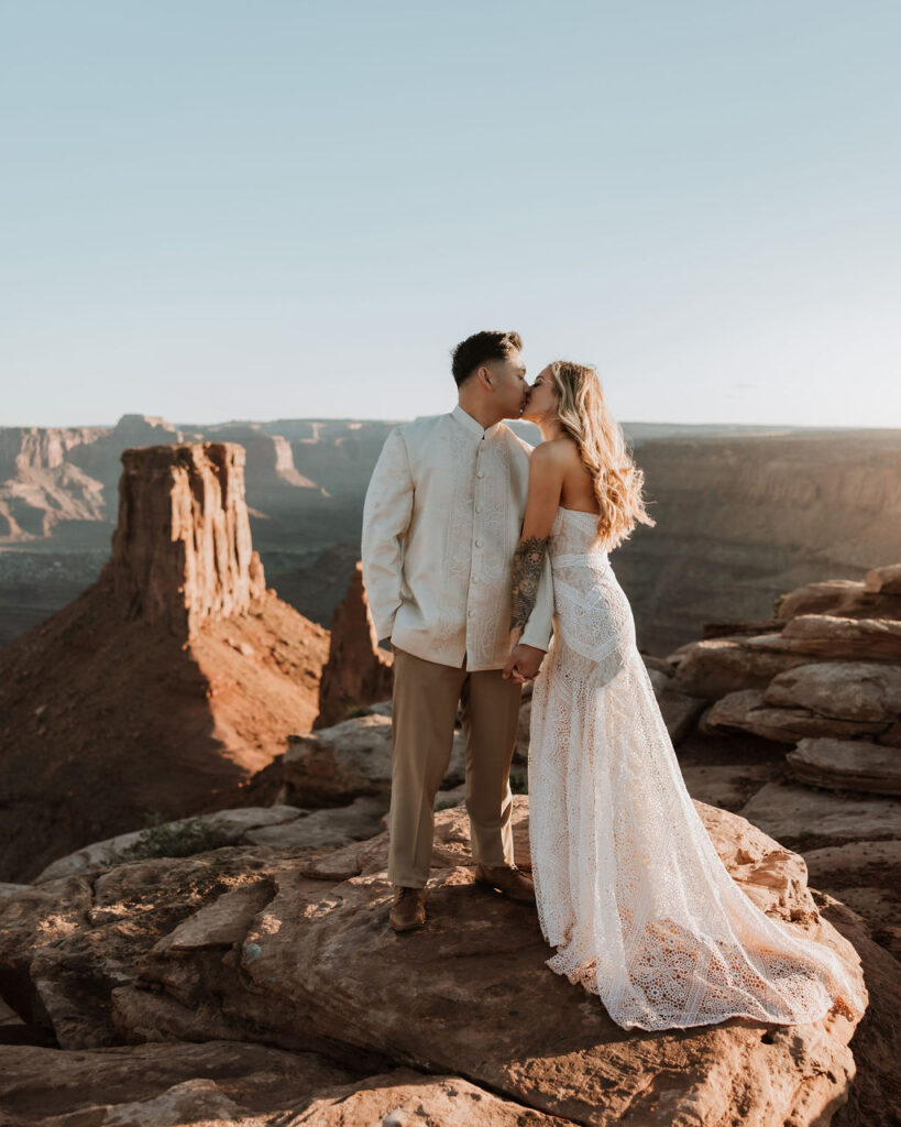 couple kiss along ledge overlooking Moab's rocky landscape