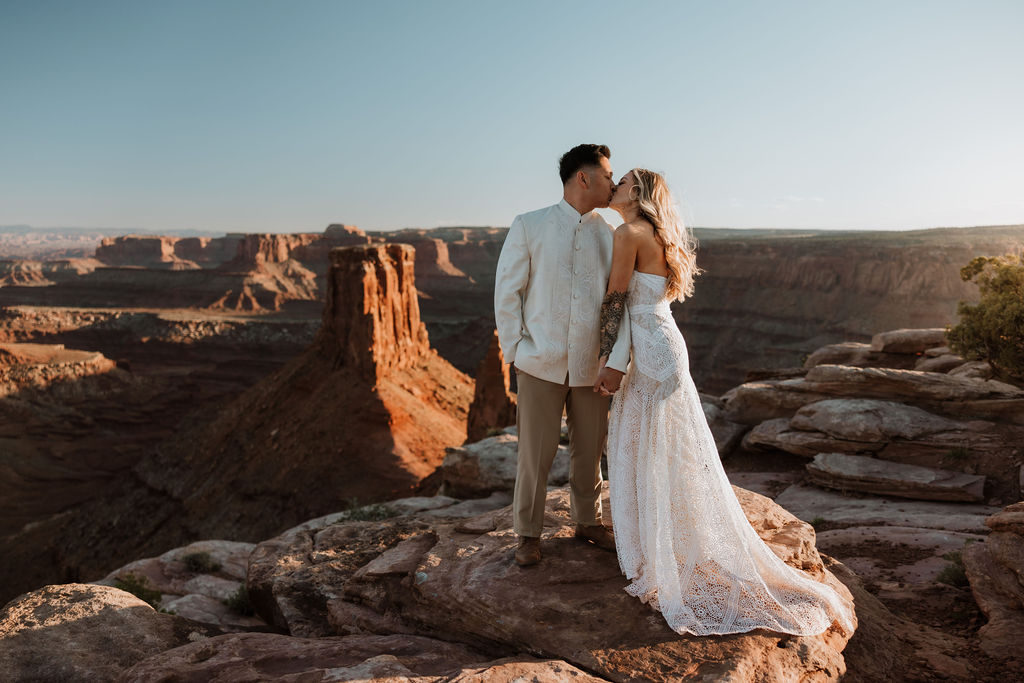 couple kiss along ledge overlooking Moab's rocky landscape