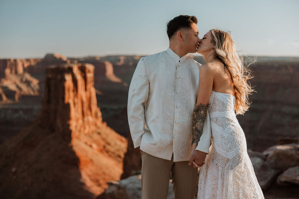 couple kiss along ledge overlooking Moab's rocky landscape
