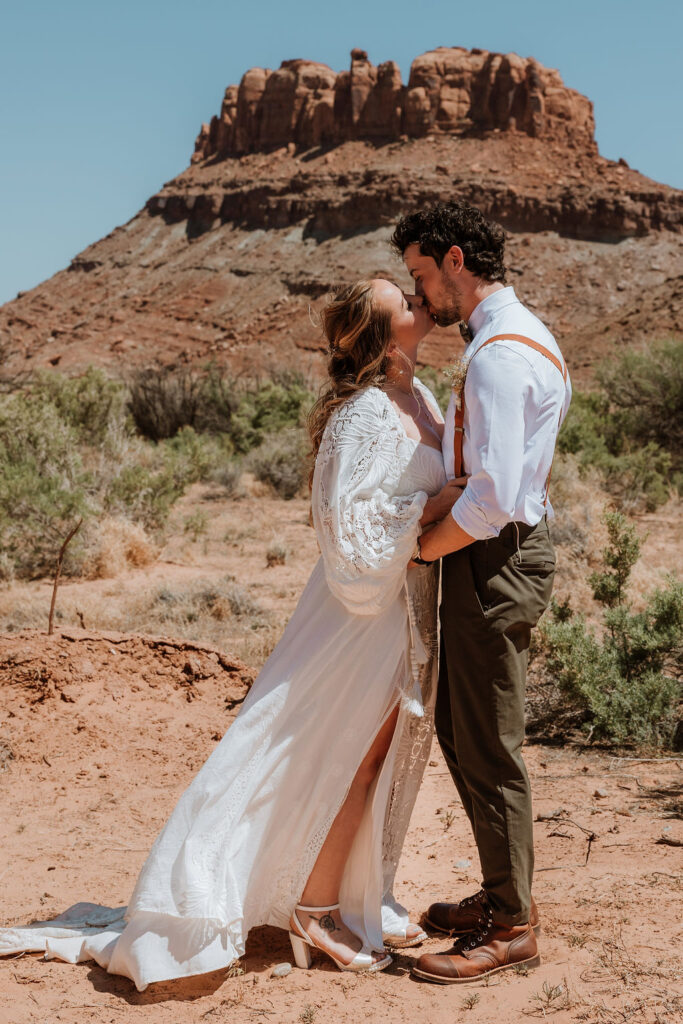 couple kisses in front of rock structure of Moab desert