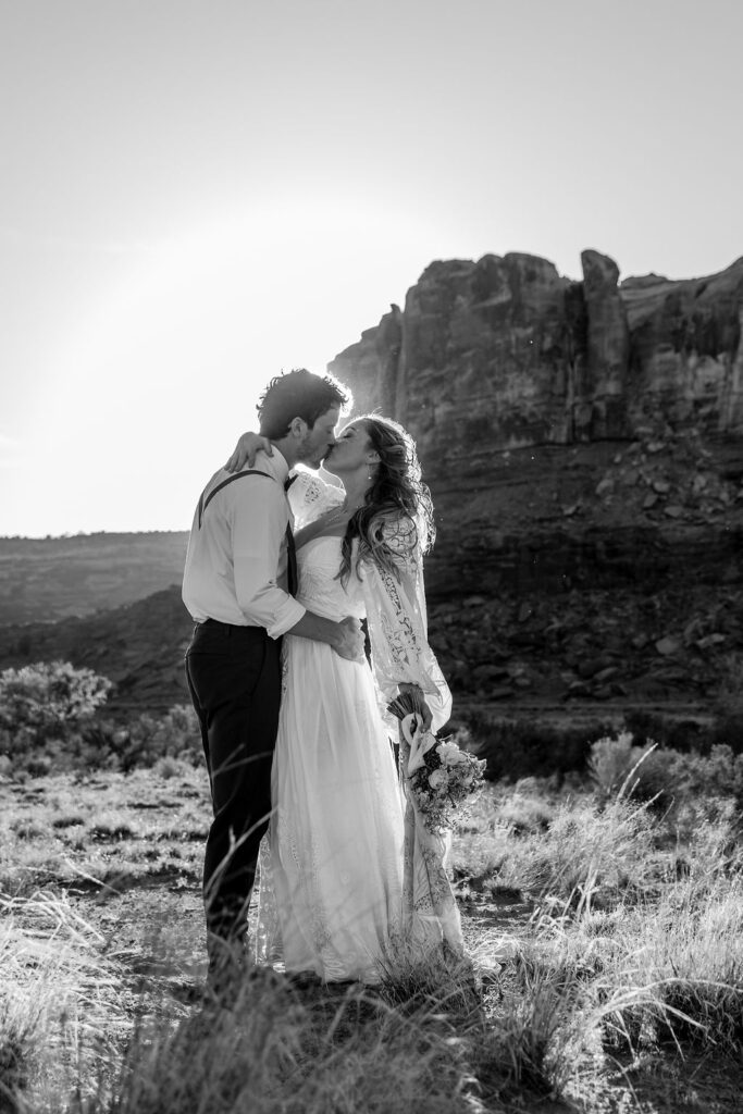 couple kisses in front of rock structure of Moab desert at sunset