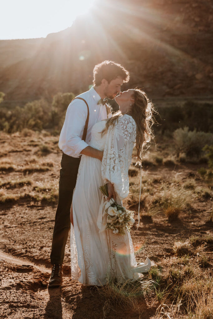 couple kisses in front of rock structure of Moab desert at sunset