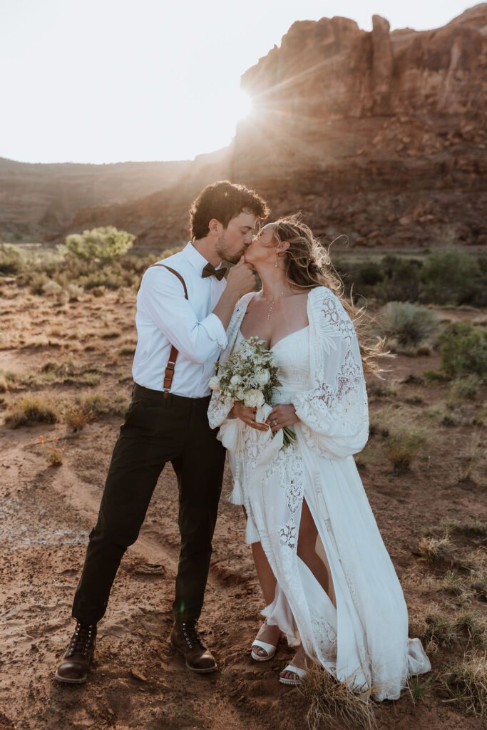 couple kisses in front of rock structure of Moab desert at sunset