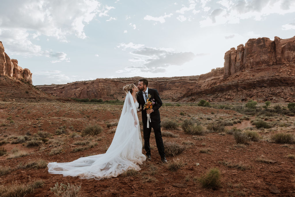 couple kiss surrounded by Moab's rocky red landscape 