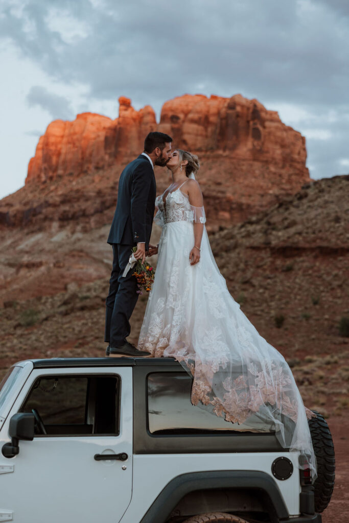 couple kissing standing on top of jeep