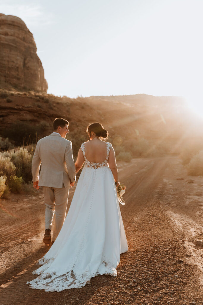 couple holding hands walking along rocky path during sunset