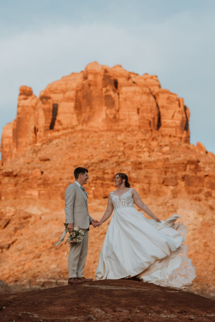 couple holding hands in front of large rock formation 