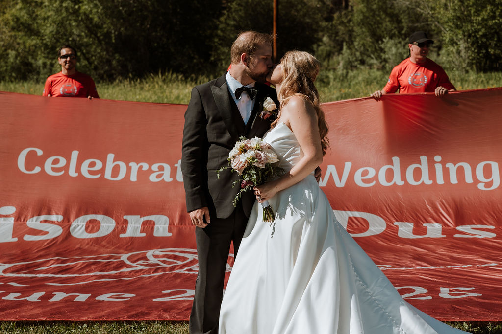 couple kiss in front of wedding sign that the parachute team had