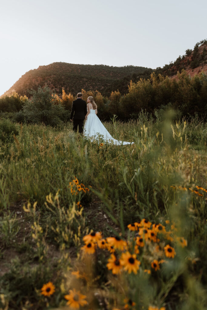 couple holding hands walks along grassy meadows of Spring Creek Ranch