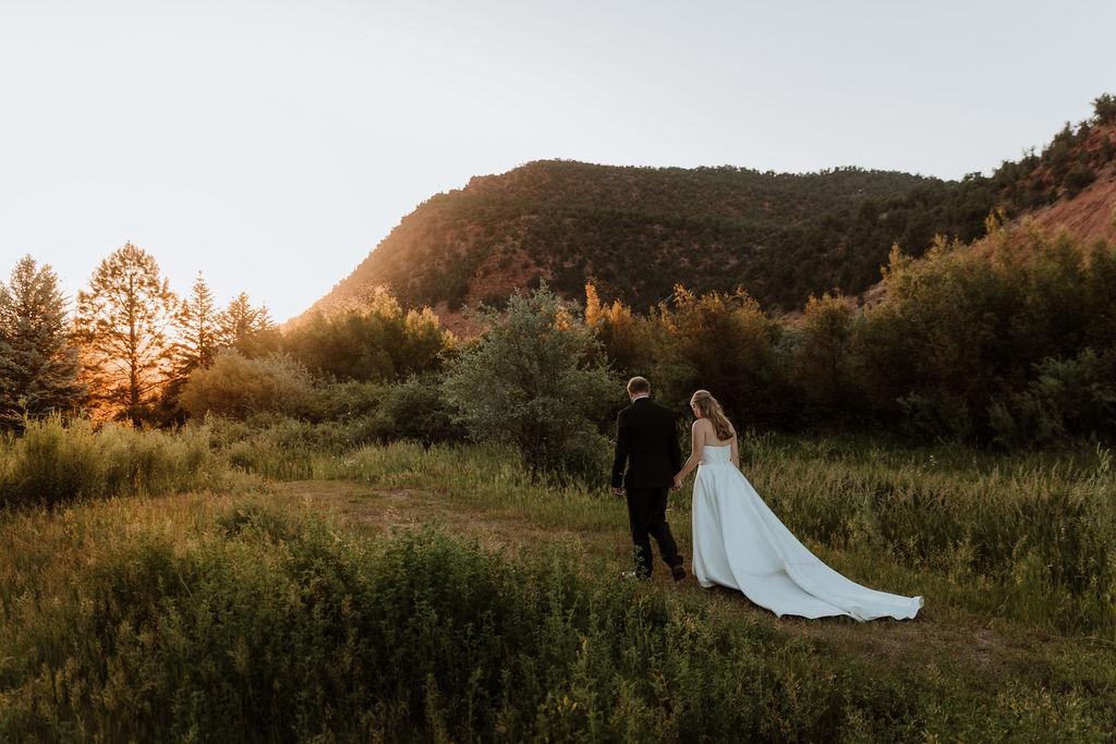 couple holding hands walks along grassy meadows of Spring Creek Ranch