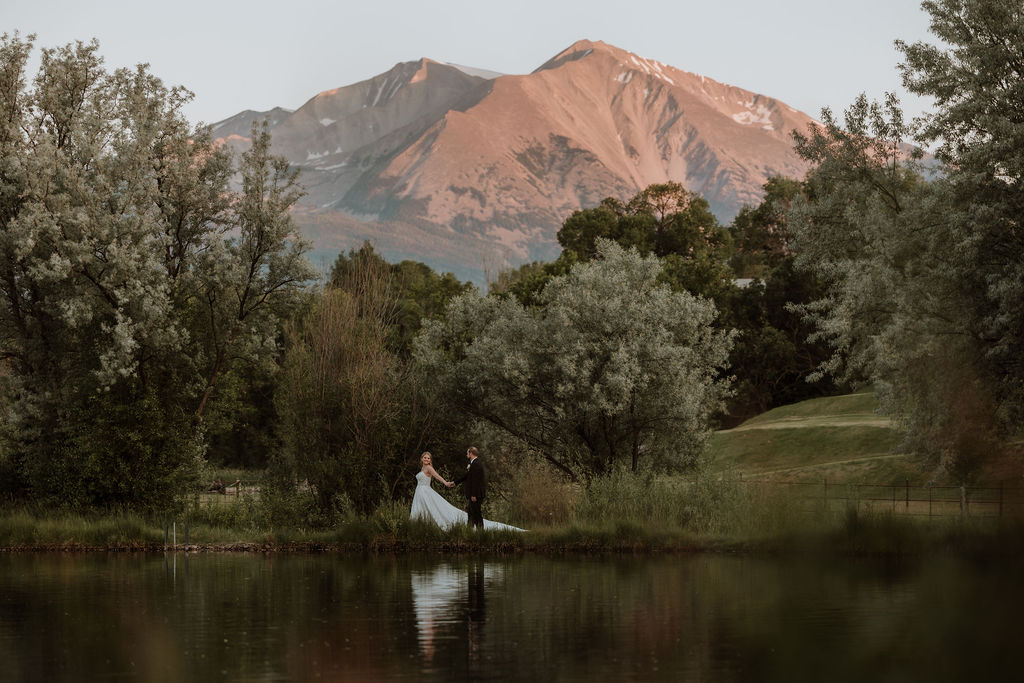 couple walk along pond with mountains in background at Spring Creeks Ranch