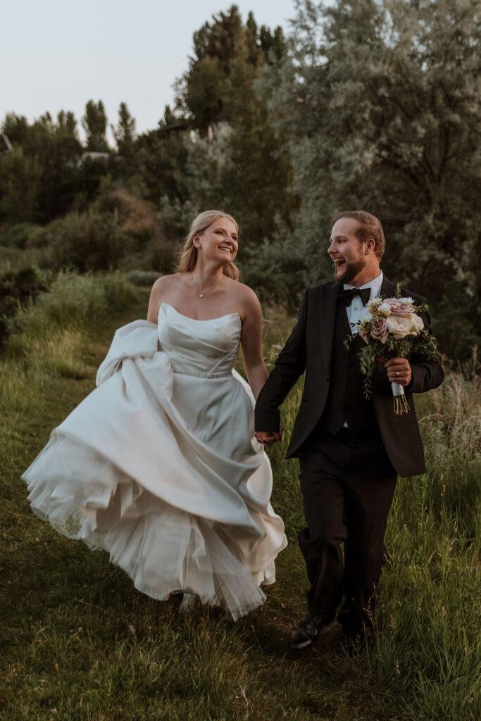 couple running and laughing along grassy path at Spring Creeks Ranch