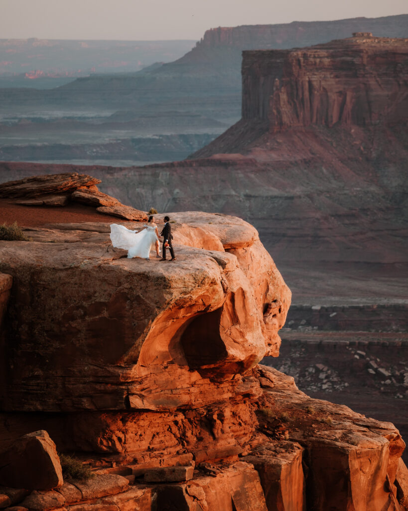 couple stands along rocky ledge of Moab during sunset
