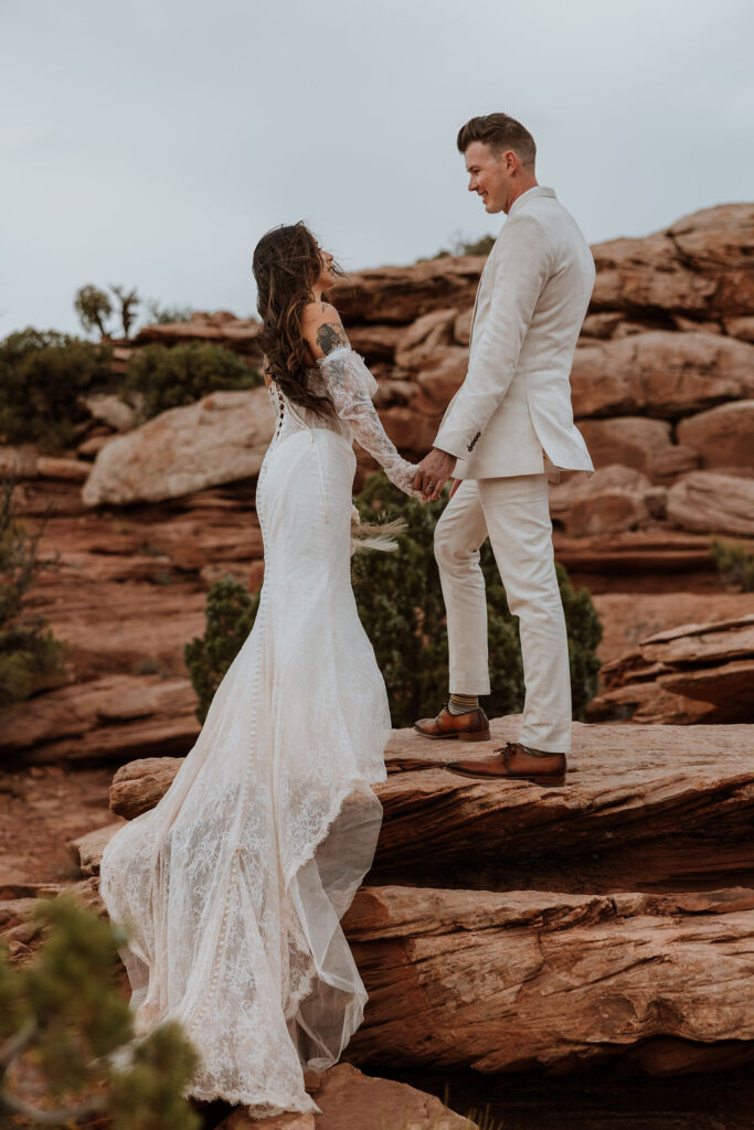 couple holds hands while standing on rocky ledge