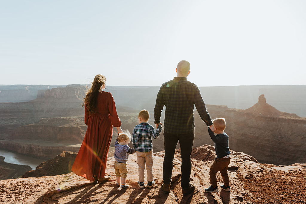 family stands along rocky ledge of Moab during sunset