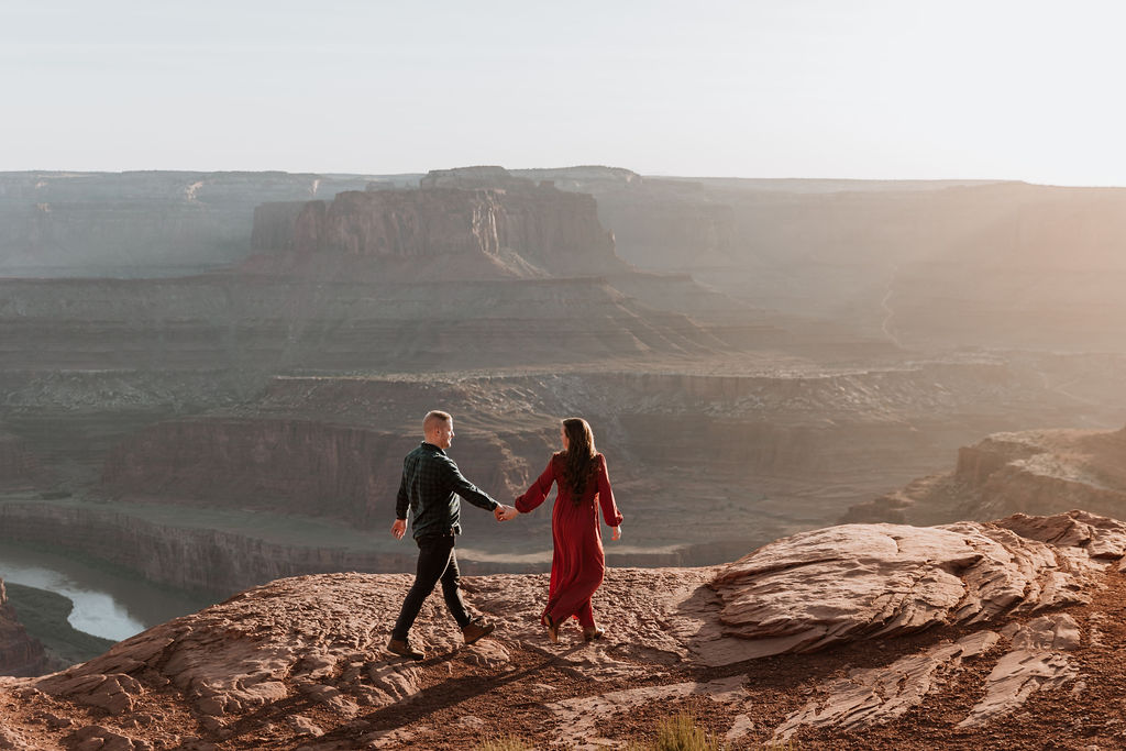couple walks along rocky ledge during sunset in Moab