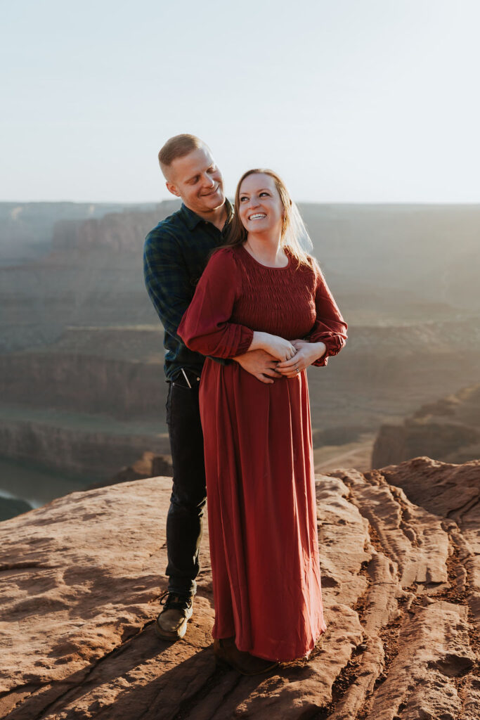couple embrace on rocky ledge overlooking Moab