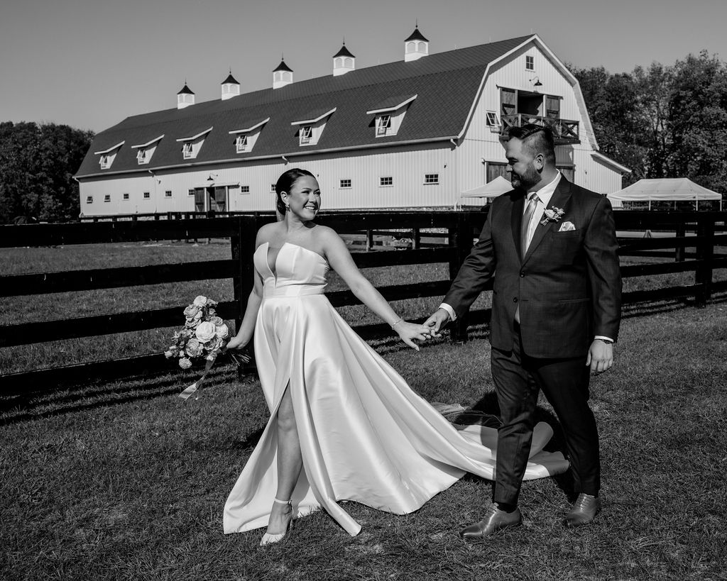 couple walks holding hands in front of barn venue
