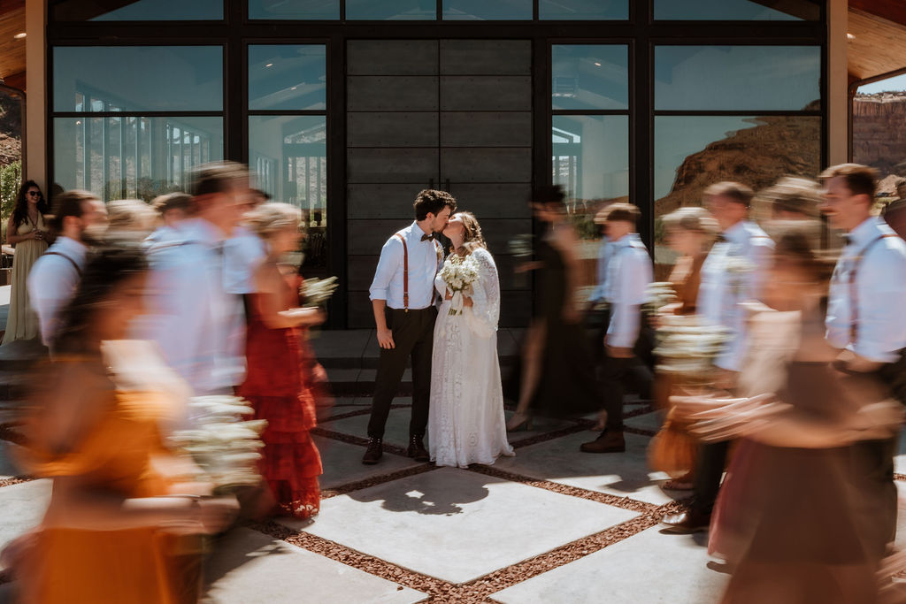couple kiss while wedding party is blurred in the background