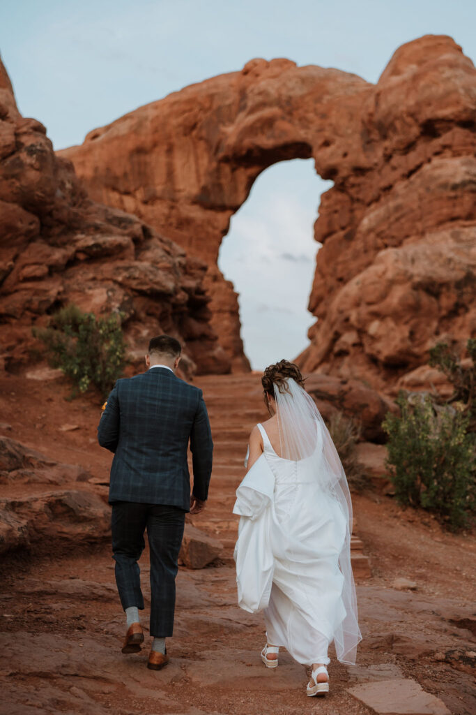 couple walk up rocky path of Arches National Park